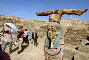 A statue showing Petah Sakar, the god of the cemetary, that was found recently, stands at right as Egyptian workers carry an ancient wooden coffin shaped like a human body that dates back to the 26th Pharaoh Dynasty that ruled from 672 BC to 525 BC, in Sakkara, south of Cairo Wednesday, March 2, 2005. Australian archaeologists have discovered one of the best preserved ancient Egyptian mummies dating from about 2,600 years ago, Zahi Hawass, the head of Egypt's Supreme Council for Antiquities said. (AP Photo/Amr Nabil)